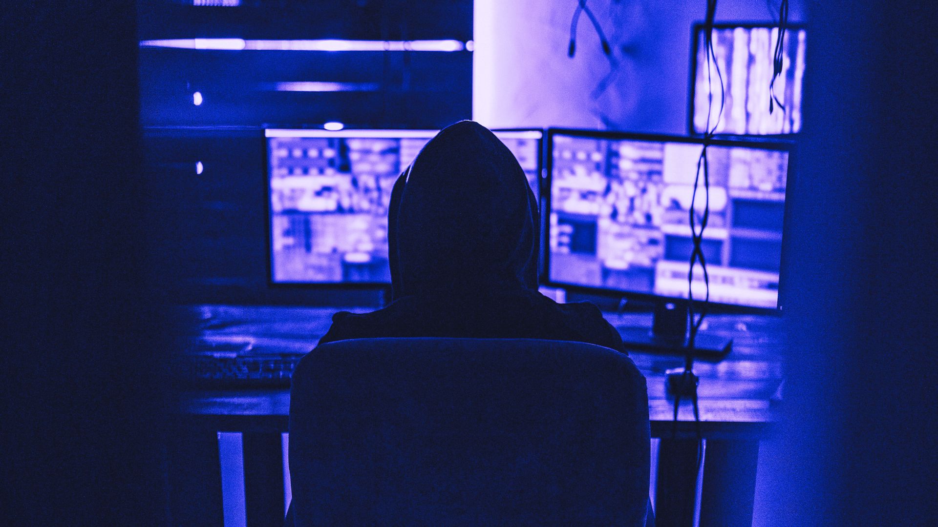 hacker sitting in basement with multiple screens